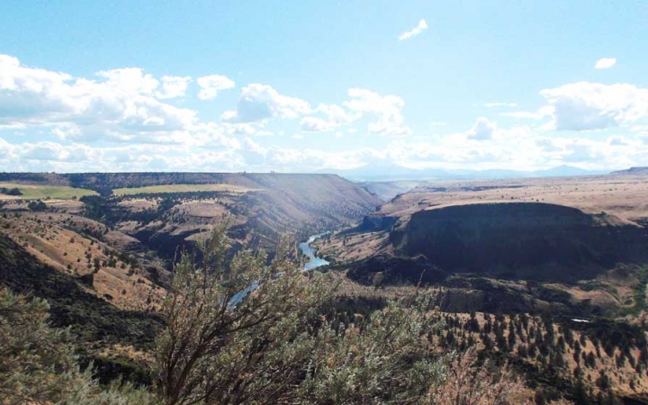 a river flows through a vast hilly landscape under blue skies